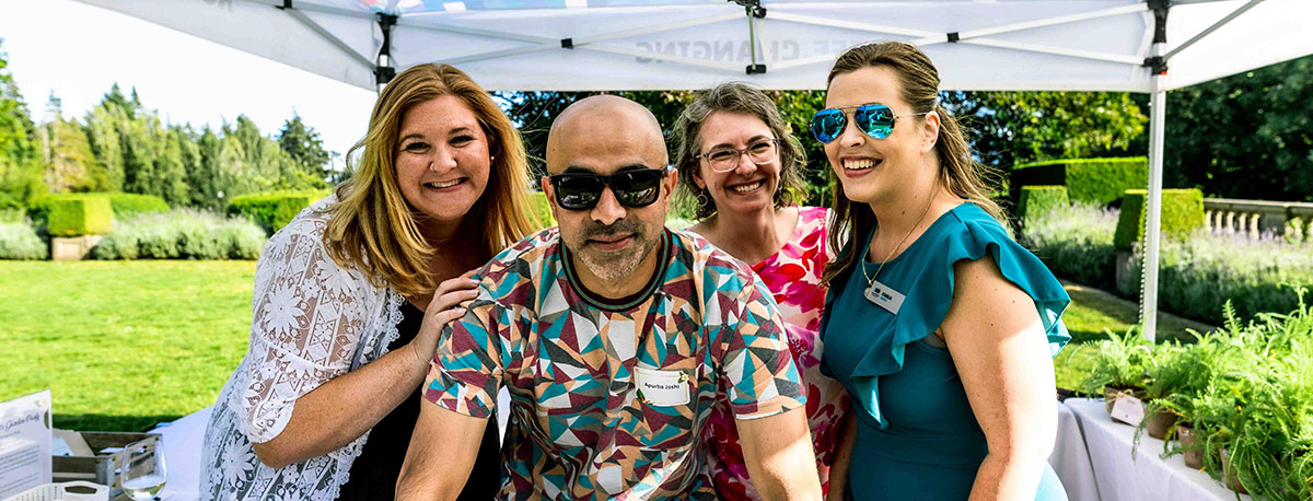 Four RRU employees stand together outdoors under an event tent, smiling for a photo