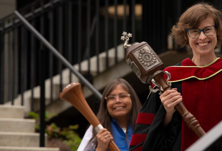 Members of the Royal Roads University community carrying maces and smiling outdoors.
