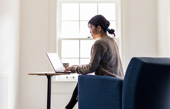 Person sitting at a workstation at home, typing on a laptop