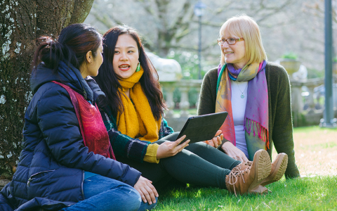 Three people sitting by a tree on RRU campus