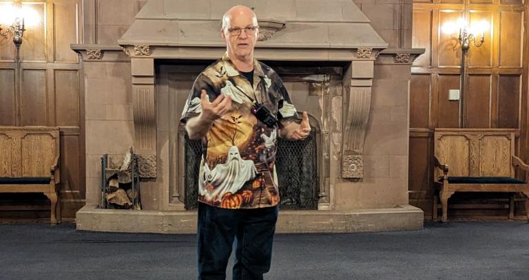 Man standing in front of a large fireplace wearing a shirt with ghosts printed on it.